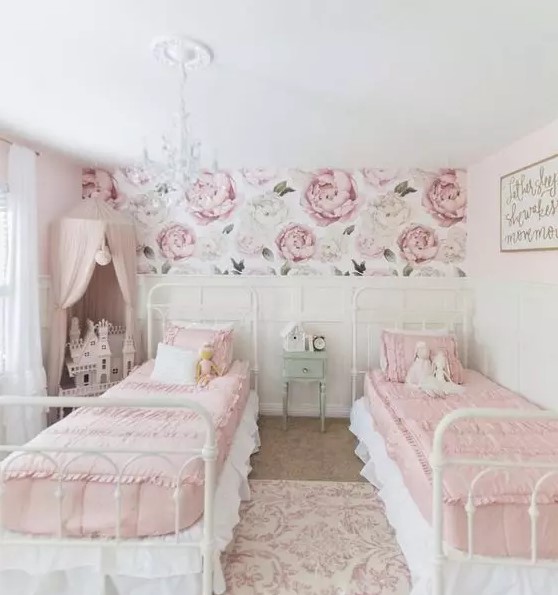 a sophisticated shared girls' bedroom with white metal beds, pink and white bedding, white paneled walls, a pink canopy over a doll house