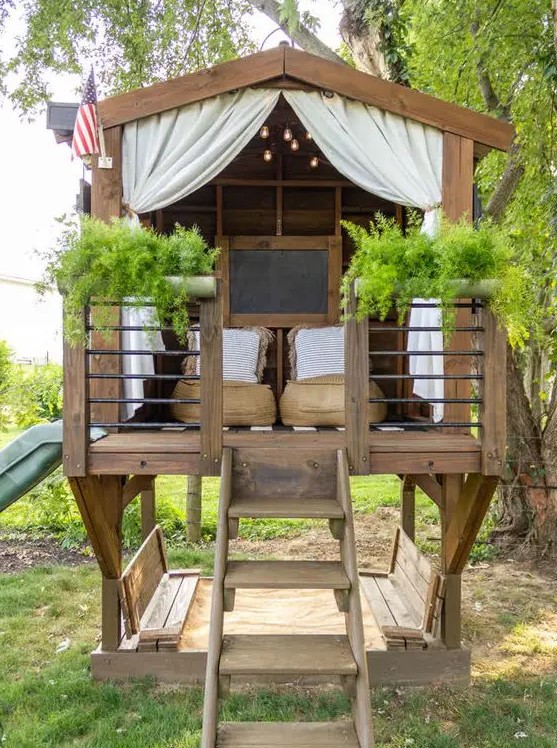 a stained kids' playhouse with low chairs, potted greenery, lights, a chalkboard and a ladder will be great for adults, too