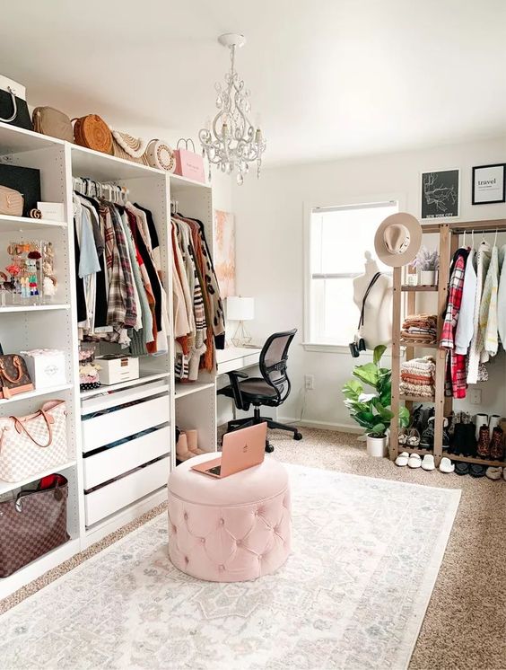 a stylish and girlish cloffice with a white desk, a black chair, a pink storage pouf, open storage units, a makeshift closet and drawers for clothes