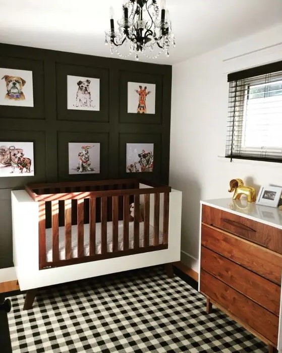 a stylish mid-century modern nursery with a black accent wall with a gallery wall, a white crib, a stained dresser, a buffalo check rug and a black chandelier