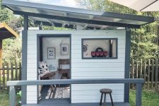 a stylish modern kids’ playhouse painted grey and white, with a porch and some lovely furniture and art inside is a cool solution