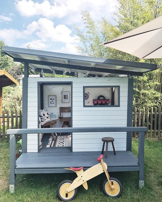 a stylish modern kids' playhouse painted grey and white, with a porch and some lovely furniture and art inside is a cool solution