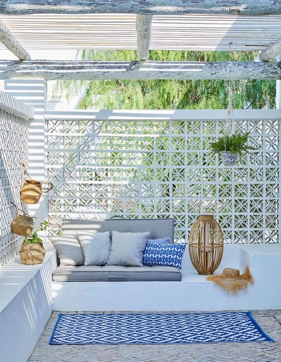 a stylish sea themed terrace with built in concrete furniture, grey andblue pillows and rugs, some potted plants