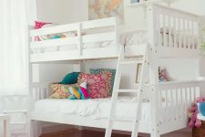a stylish white shared girls’ bedroom with a bunk bed, colorful pillows, white stools, a hot pink printed rug, colorful toys, decor and details