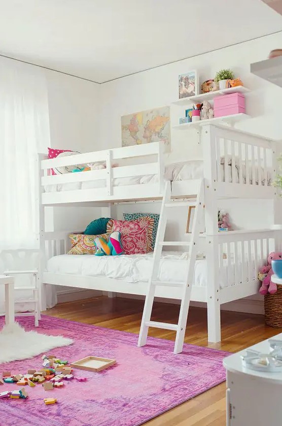 a stylish white shared girls' bedroom with a bunk bed, colorful pillows, white stools, a hot pink printed rug, colorful toys, decor and details