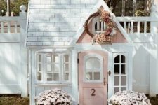 a super cute white and pink kids’ playhouse with windows, potted blooms and pumpkins outside and a floral wreath is wow