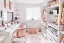 a super pretty and glam cloffice with a large desk vanity, open storage units and some drawers, pink suitcases and a unique chandelier