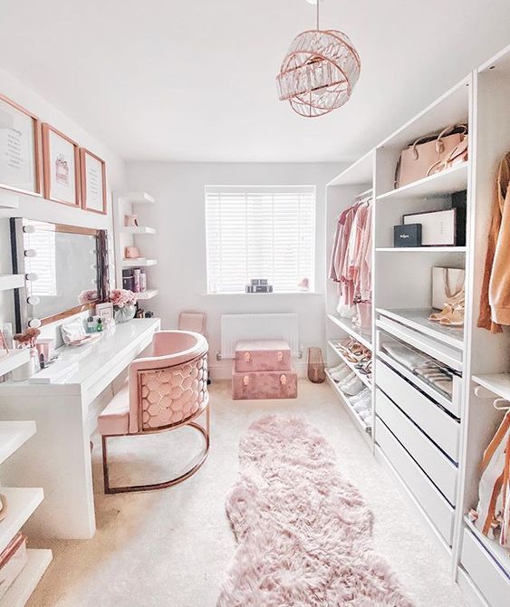 a super pretty and glam cloffice with a large desk vanity, open storage units and some drawers, pink suitcases and a unique chandelier