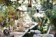 a super welcoming garden dining space under the trees, with lights and candle lanterns, two wooden tables and mismatching chairs