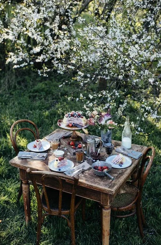 a vintage rustic dining space with shabby chic wooden furniture placed right under the blooming trees