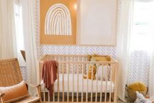 a warm-colored mid-century modern meets boho nursery with printed wallpaper, stained furniture, layered rugs, mustard pillows, a woven pendant lamp