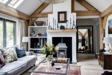 a welcoming barn living room with wooden beams, a vintage hearth, grey seating furniture, a glass sofa, various accessories