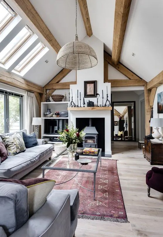 a welcoming barn living room with wooden beams, a vintage hearth, grey seating furniture, a glass sofa, various accessories