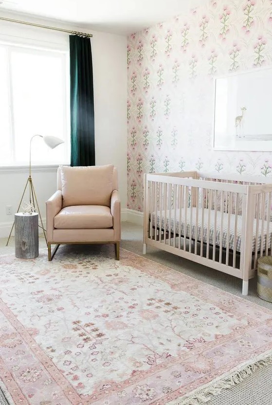 a welcoming neutral mid century modern nursery with a tan crib, a tan chair, printed layered rugs, printed wallpaper, dark green curtains, a side table