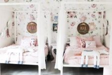 a whimsy shared girls’ bedroom with a floral wallpaper wall, white beds with canopies, a nightstand, pink bedding, a rug and a pouf is wow