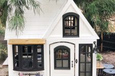 a white and black kids’ playhouse with potted blooms and greenery is a lovely idea for a modern farmhouse backyard