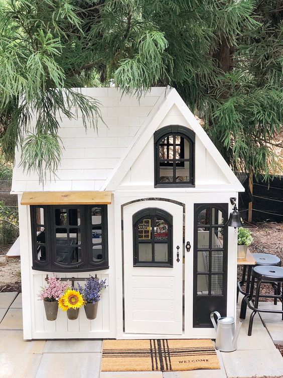 a white and black kids' playhouse with potted blooms and greenery is a lovely idea for a modern farmhouse backyard