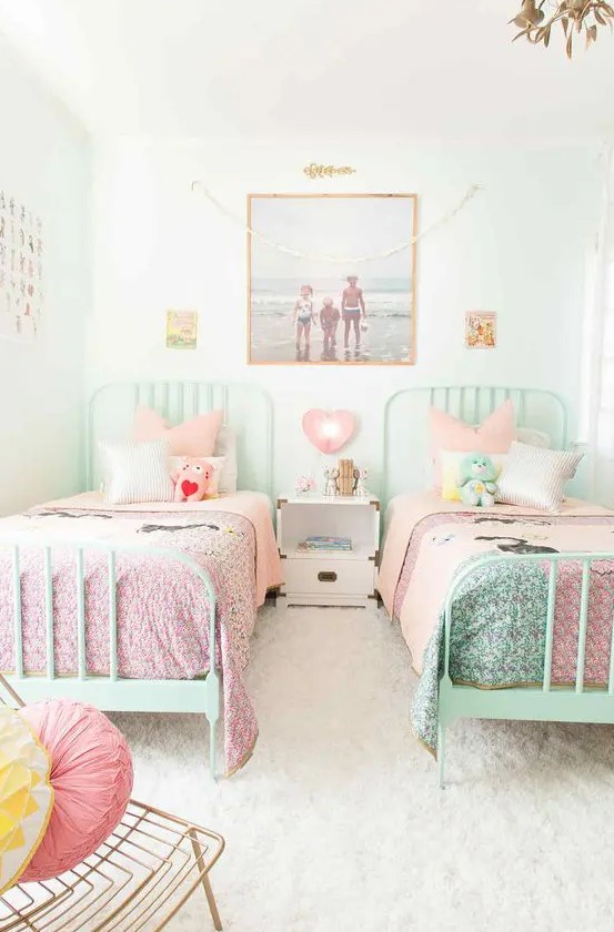 a white shared girls' bedroom with mint beds and pink and mint bedding, a gallery wall, a white nightstand, a gold chair with bright pillows