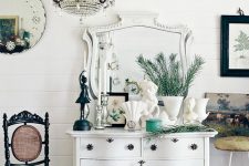 a white vintage dresser with vintage handles and knobs, with some vintage decor, candleholders and vases with evergreens