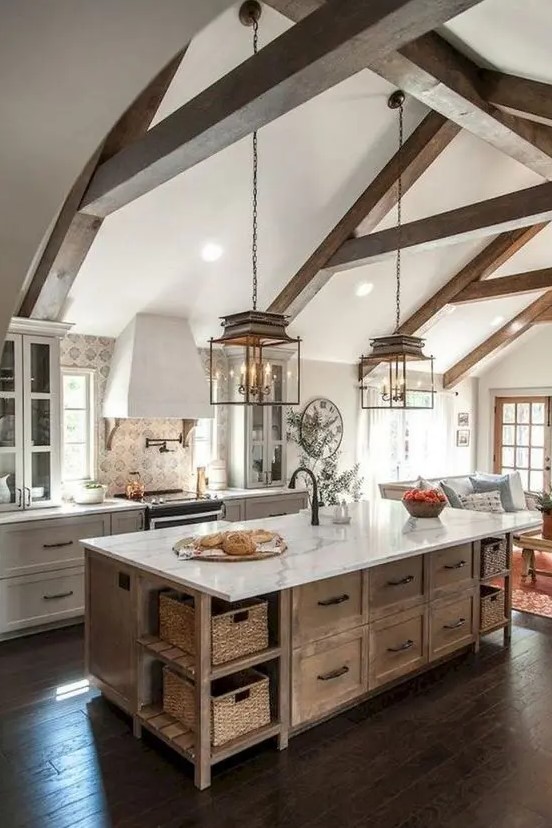 an elegant barn kitchen with wooden beams, white shaker style cabinets, a stained kitchen island, vintage pendant lamps