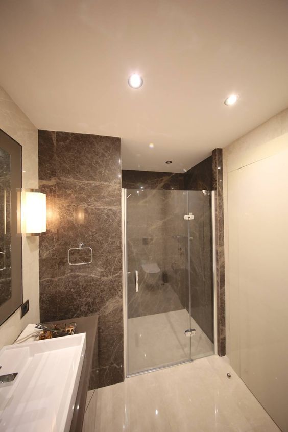 an elegant bathroom with brown marble tiles in the shower space, a floating vanity with a sink and lots of light