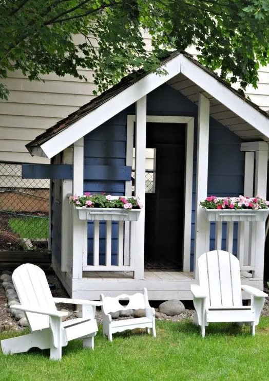 an elegant blue and white kids' playhouse with potted bold blooms and some white garden furniture next to the house