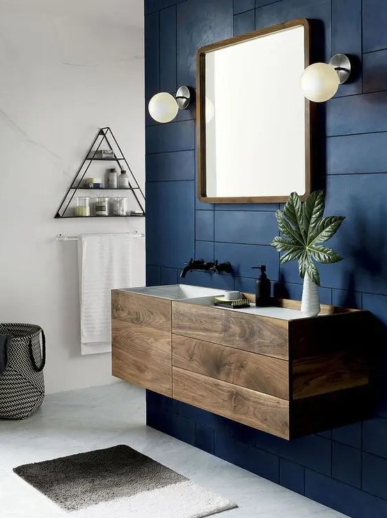 an elegant dark stained bathroom vanity with drawers looks very eye catchy on a contrasting navy patterned wall and adds interest to the space