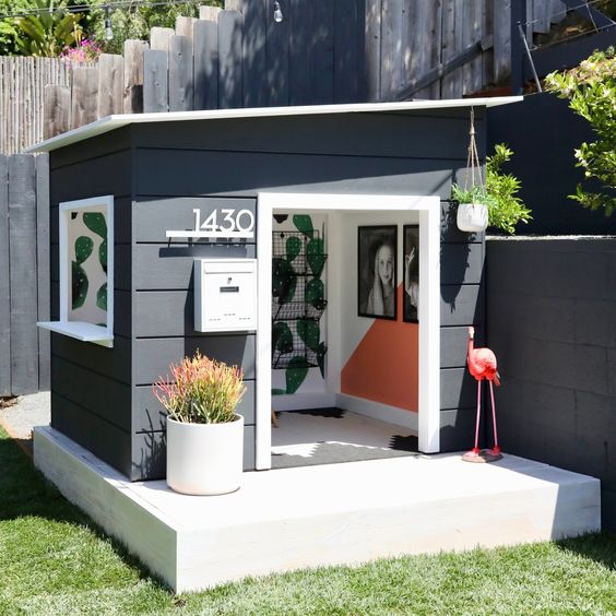 an elegant modern playhouse painted black and white, with a window, some lovely decor inside and potted plants is super cool