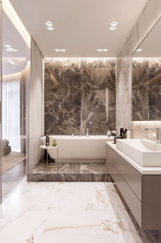 an exquisite bathroom done with marble tiles, with tan and white ones, a bathtub on a platform and a long vanity
