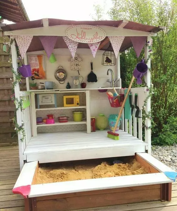 an outdoor kids' play kitchen with an additional sand box that can be hidden as it's a drawer or pulled out when needed