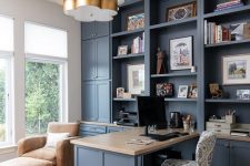 02 a blue home office with shaker cabinets, a stone countertop on the built-in desk, a leather chair with a footrest and a chic gilded chandelier