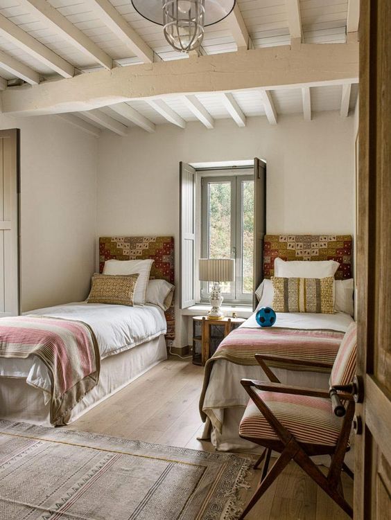 a boho rustic shared guest bedroom with patchwork headboards, neutral bedding and a lovely chair next to them