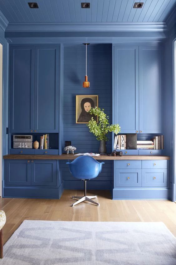 a bold blue home office done with large kitchen cabinets, a built-in desk and a pendant lamp, a printed rug