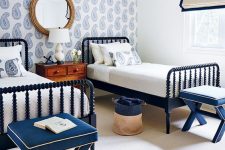 04 a bold nautical shared guest bedroom with a blue printed wallpaper wall, navy wooden beds and stools, a stained nightstand
