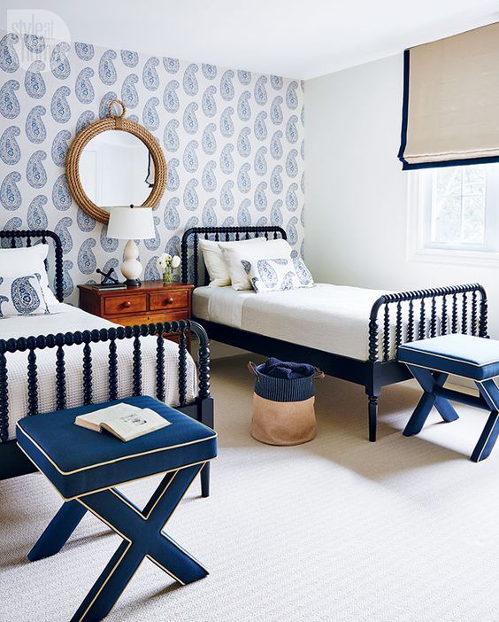 a bold nautical shared guest bedroom with a blue printed wallpaper wall, navy wooden beds and stools, a stained nightstand