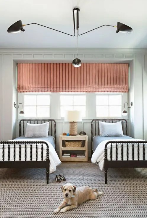 a chic shared guest bedroom with a triple window covered with a coral shade and a printed rug