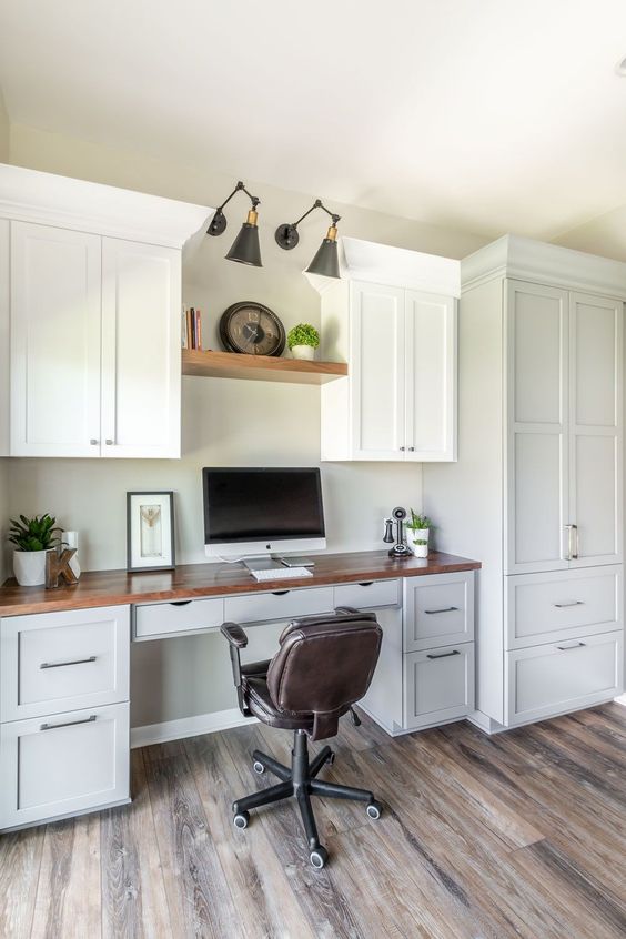 a cozy white home office fully done wiht grey and white kitchen cabinetry, a stained countertop, an open shelf, black sconces and a dark chair