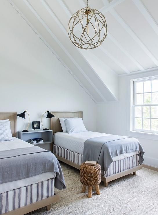 a coastal shared bedroom with matching light-stained beds with blue bedding, a jute stool and black table lamps