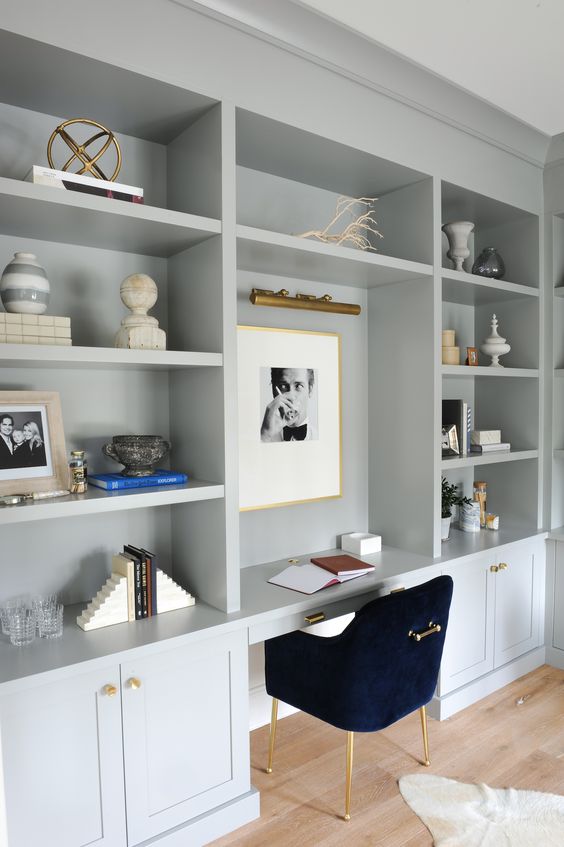 a dove grey farmhouse home office with shaker style cabinets, open storage compartments, a black chair and touches of brass