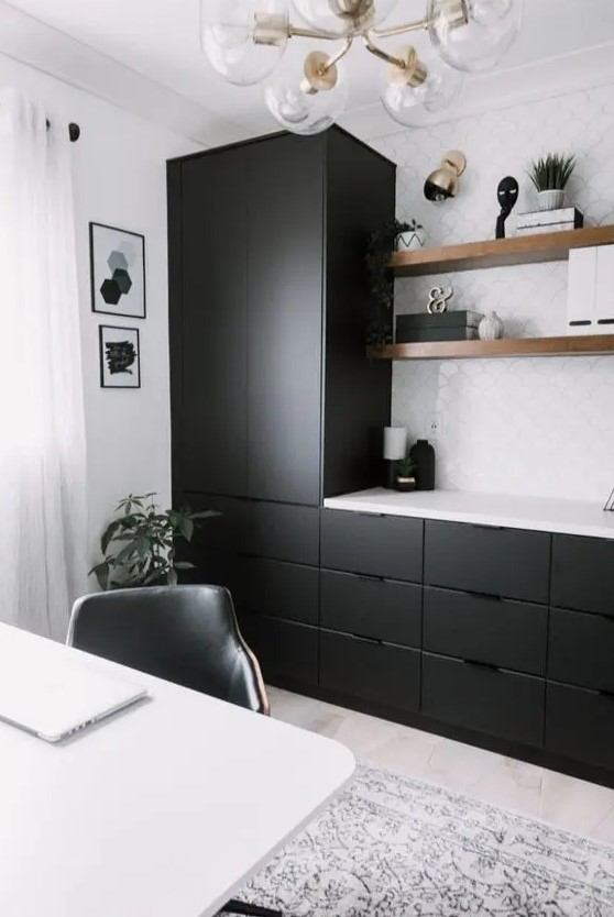 a modern home office with sleek black cabinets and a white tile backsplash, floating shelves and a white desk plus a retro chandelier