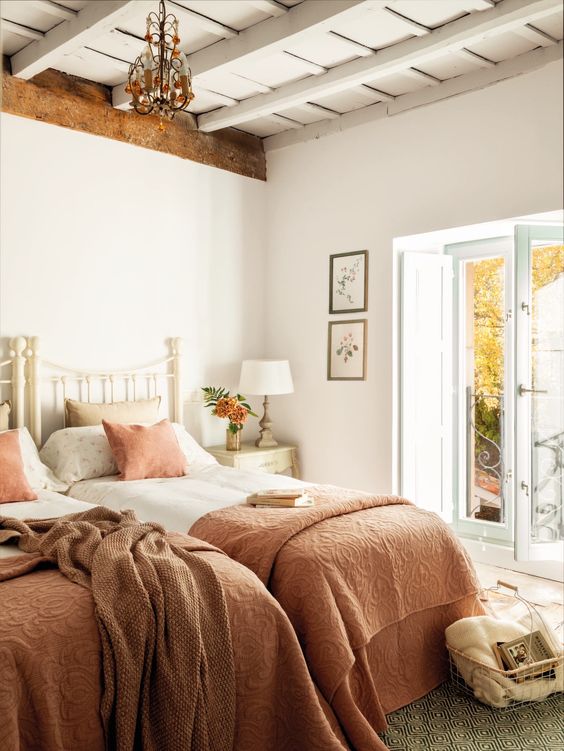 a cozy rustic shared guest bedroom with white metal beds and pastel bedding, a chic chandelier and a view of the garden