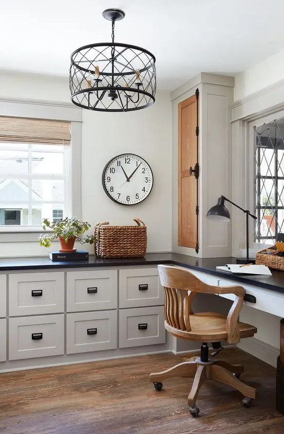 a stylish farmhouse home office done with pretty kitchen cabintery and a built in desk, a wooden chair, a metal chandelier and a basket