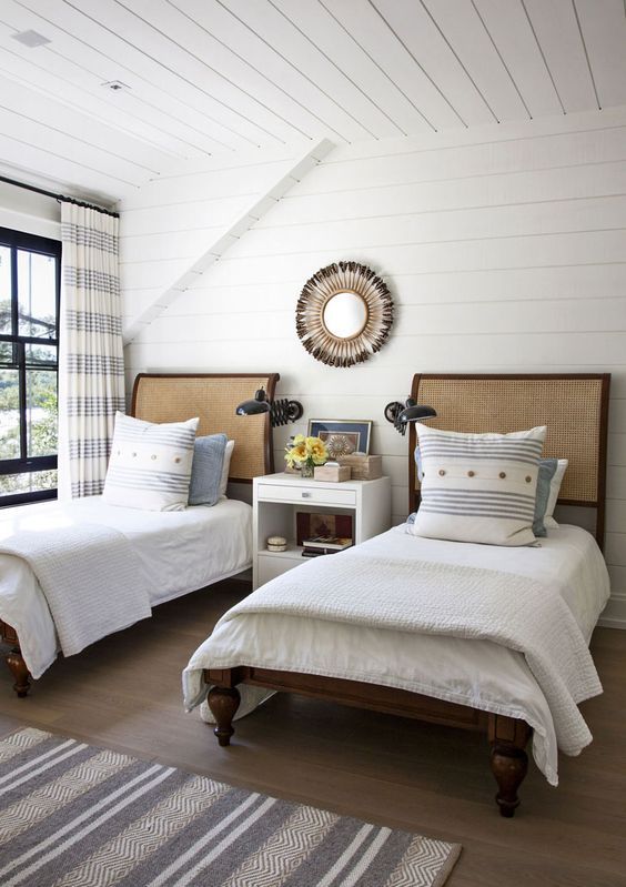 a farmhouse bedroom with planked walls and a ceiling, dark-stained beds with neutral bedding, a white nightstand and printed textiles
