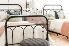 16 a farmhouse guest bedroom with two metal beds and touches of various muted colors, a polka dot pouf and black sconces over each bed