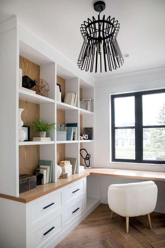 a white farmhouse kitchen with shaker cabinets and open storage units, a built in desk and a creamy chair, a black chandelier
