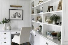 17 a white farmhouse kitchen with shaker scabinets, open storage units, a built-in desk and a creamy chair plus greenery