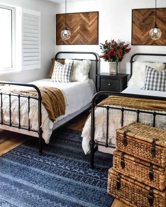 a farmhouse shared guest bedroom with black metal beds with neutral bedding, stacked woven suitcases and wooden headboards