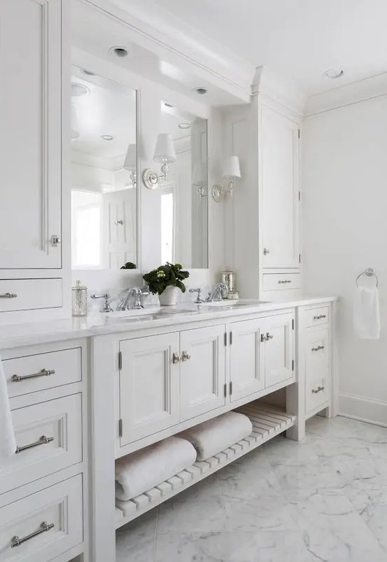 a gorgeous master bathroom with creamy shaker style cabinets from the kitchen, a double mirror and sink, sconces and a chic floor