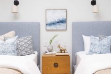 22 a lovely coastal shared guest bedroom with blue upholstered beds, neutral bedding, a stained nightstand and sconces