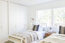 23 a mid-century modern neutral shared guest bedroom with a couple of wardrobes, white beds with neutral bedding,a  striped rug and green stools